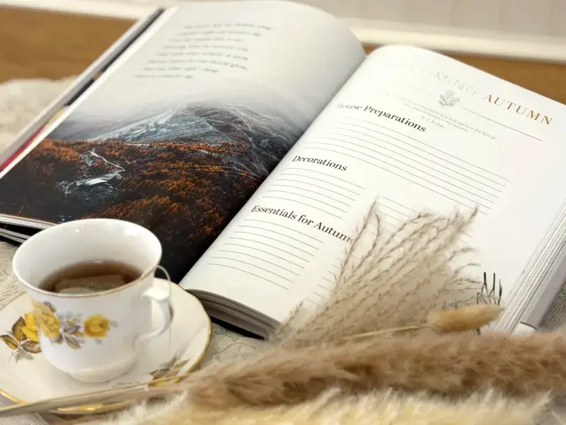 The Harvest book open to Welcoming Autumn, with blank writing spaces beside a cup of tea and dried grasses.